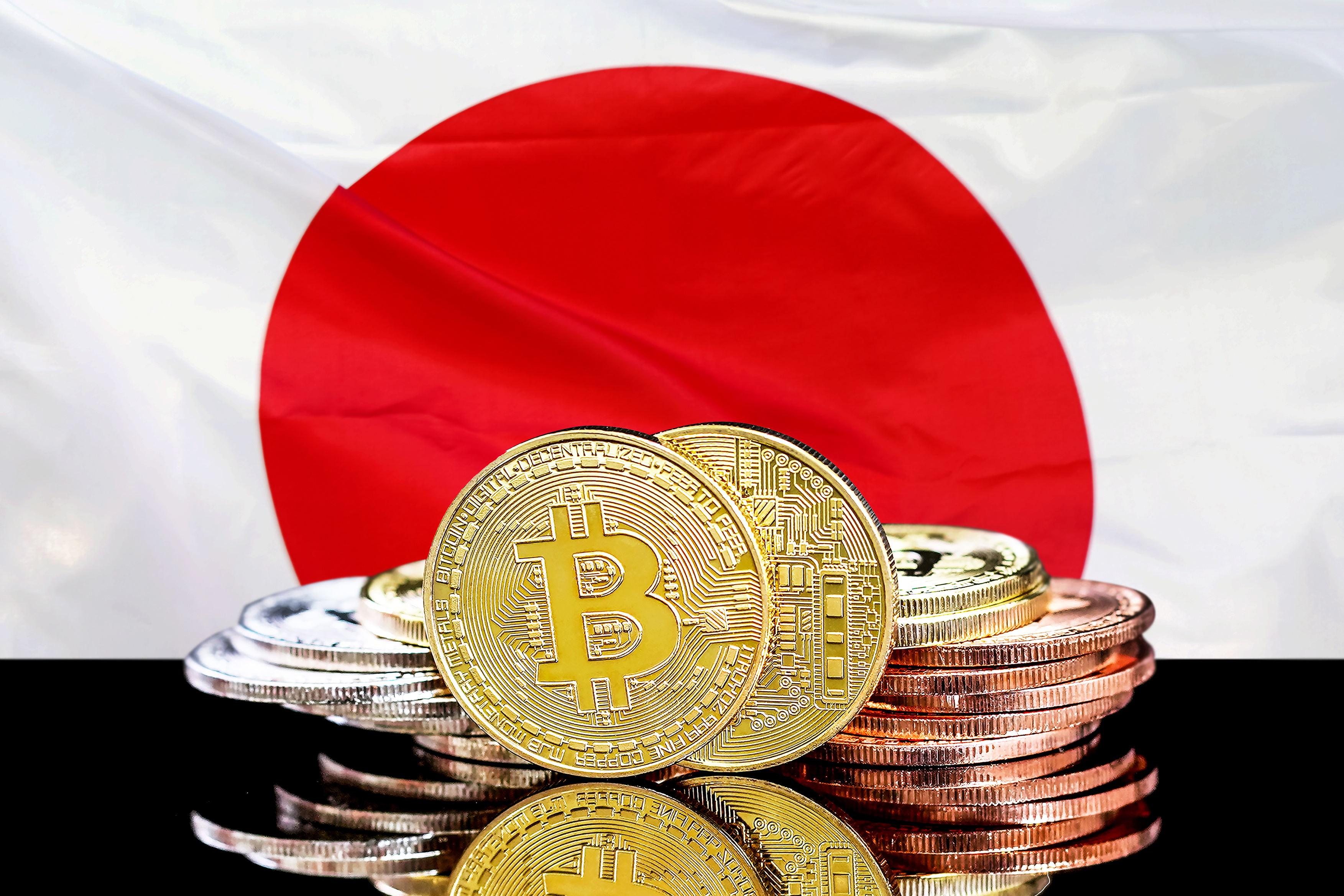 A pile of tokens representing cryptocurrencies rest on a table in front of the Japanese flag.