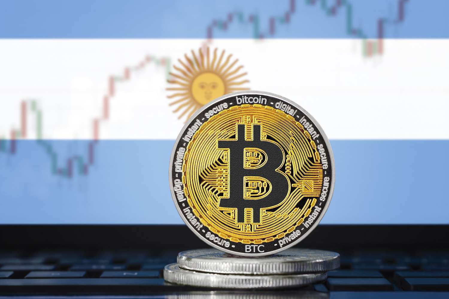Металлические токены, символизирующие биткоин на фоне флага Аргентины и графика цен.